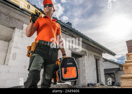 Proud Construction Worker with a Spirit Level on His Shoulder and Tool Box in a Hand. Construction Industry Theme. Stock Photo