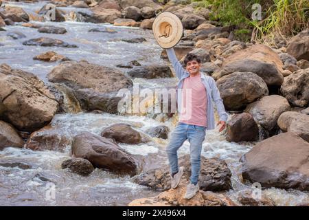 lifestyle. very happy young latin man on the rocks of the river waves with hat in hand Stock Photo