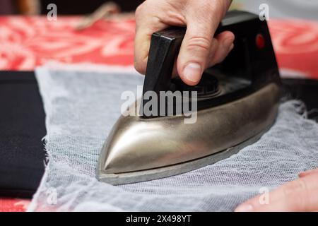 Using their thumb and fingers, a person irons a piece of fabric on a wooden table. The ironing board is covered with carmine leather, a fashionable ch Stock Photo