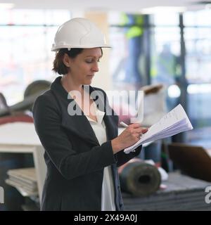 Construction, document and serious woman or architect writing notes for industrial building development project manager. Paperwork, engineer and Stock Photo