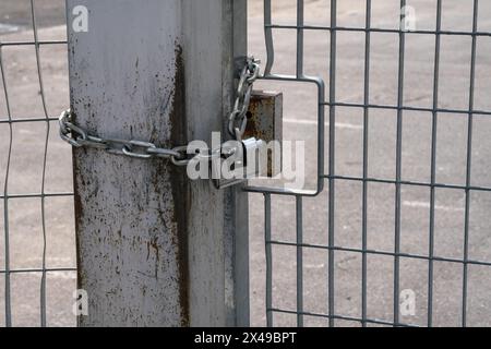 fence: pole and padlock with chain to a fence with electro-welded metal grating in stainless steel. the grill is made with a resistant and solid struc Stock Photo