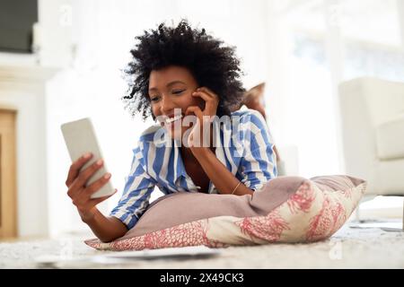 Black woman, home and smile on smartphone with lying on floor for online application or booking for traveling. Female person, living room and happy Stock Photo