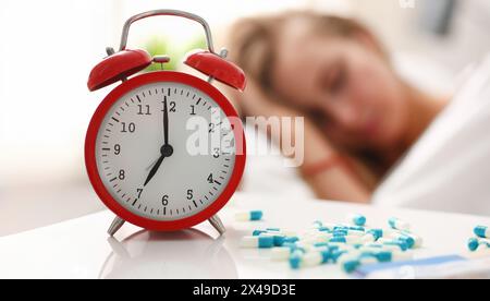 Pieces are scattered on the table near alarm clock which shows 7 am. Young woman sleeping in bed on the effects of narcotic pharmaceutical medications Stock Photo