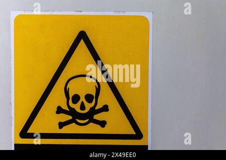 A yellow and black sign with a skull on it that says 'Peligro Intoxicacion' in Spanish Stock Photo