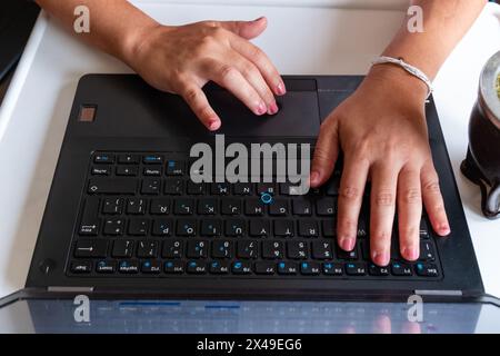 A person is typing on a laptop keyboard. The laptop is open and the screen is displaying a webpage. The person's hands are on the keyboard, and they a Stock Photo