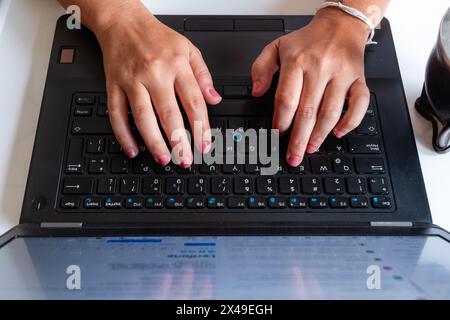 A person is typing on a laptop keyboard. The laptop is open and the screen is displaying a webpage. The person's hands are on the keyboard, and they a Stock Photo