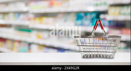 Empty shopping basket on pharmacy drugstore counter with blur shelves of medicine and vitamin supplements background Stock Photo