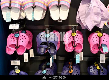 Rows of pink imitation kids clogs, sandals and hats on display in shop for summer holidays Stock Photo