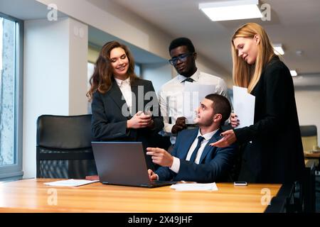 Multiethnic business team collaborates in modern office. African, Arabic, Caucasian professionals discuss strategy, celebrate success around laptop Stock Photo