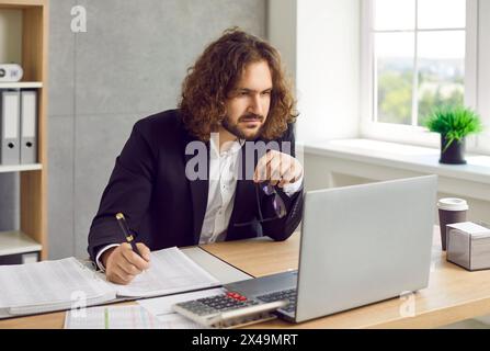 Bearded business man working at the desk on workplace at office looking at laptop monitor screen. Stock Photo