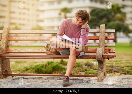 Notebook, nature and man on bench writing for college test, research and assignment studying. Reading, information and male student preparing for Stock Photo