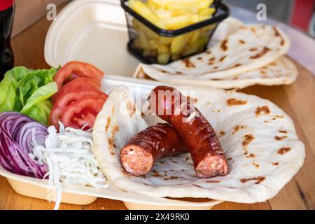 Tortilla wrap, a delightful fusion of savory sausages, crispy French fries, fresh green salad, juicy tomatoes, zesty onions, and shredded cabbage Stock Photo