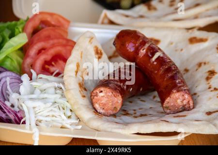 Tortilla wrap, a delightful fusion of savory sausages, crispy French fries, fresh green salad, juicy tomatoes, zesty onions, and shredded cabbage Stock Photo