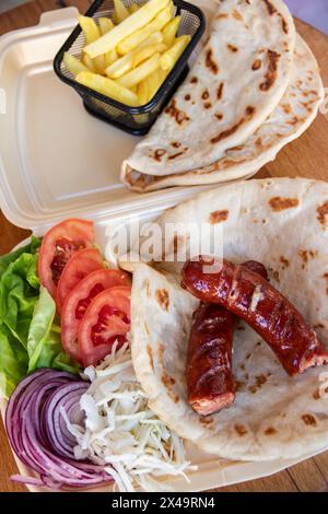 Tortilla wrap, a delightful fusion of savory sausages, crispy French fries, fresh green salad, juicy tomatoes, zesty onions, and shredded cabbage Stock Photo