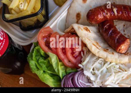 Tortilla wrap, a delightful fusion of savory sausages, crispy French fries, fresh green salad, juicy tomatoes, zesty onions, and shredded cabbage Stock Photo