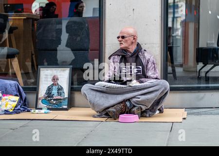 LONDON- APRIL 4th, 2024: A homeless man with a cat on Oxford Street in the West End Stock Photo
