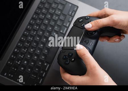 BERLIN , GERMANY - FEBRUARY 14 2024: Woman holding video controller in her hands next to MacBook Pro Stock Photo