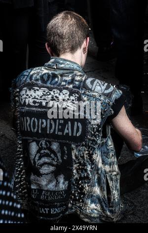 Back view of Punk Rocker in studded denim custom vest with band patches and studs sitting on the floor Stock Photo