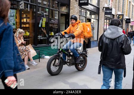 Just Eat food delivery courier cyclist riding bicycle bike on pavement outside small shops in Berwick street London England UK 2024 KATHY DEWITT Stock Photo