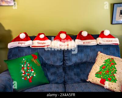 A group of five red santa hats are sitting on a blue couch. The hats are personalized with names and are arranged in a row. The couch is decorated wit Stock Photo