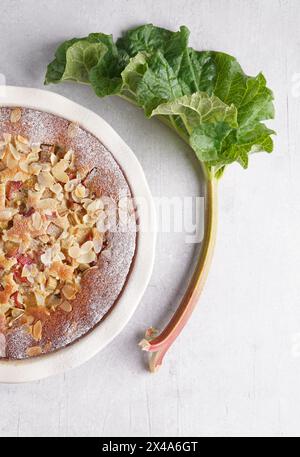 Top view of homemade round baked rhubarb pie with almonds on light table background. Rhubarb stalks on side. Seasonal spring dessert. Stock Photo