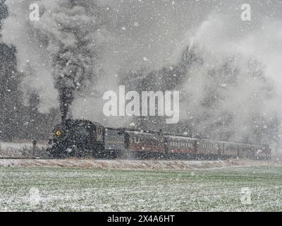 A train is traveling through a snowy field. The steam from the train is visible in the air, creating a sense of movement and energy. The scene evokes Stock Photo