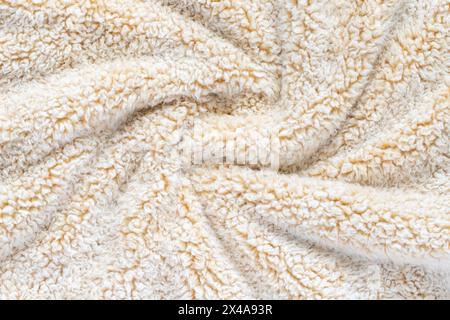 Beige soft plush fabric of comfy throw. Swirled warm blanket background. Stock Photo