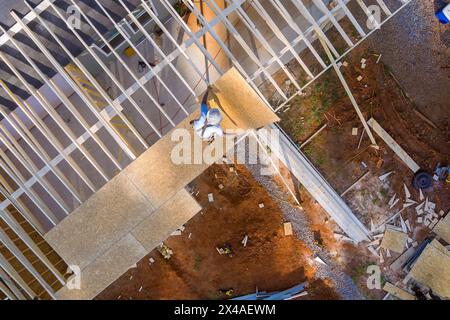 At construction site, worker hammers nails into OSB plywood panels in roof Stock Photo