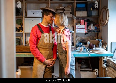 Happy couple carpenters kissing at workplace. Spouses holding hands laughing smiling expressing love Stock Photo