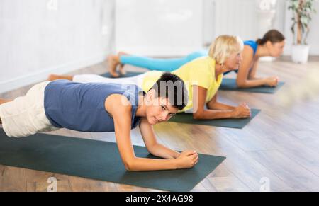 Mother, grandmother and adolescence son do exercise elbow plank pose Sampatasana. Stock Photo