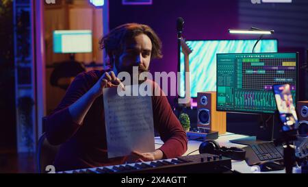 Guitar teacher recording online music lesson on smartphone, showing musical sheet with notes and accords. Musician providing detailed explanations of the theory behind each string. Camera A. Stock Photo