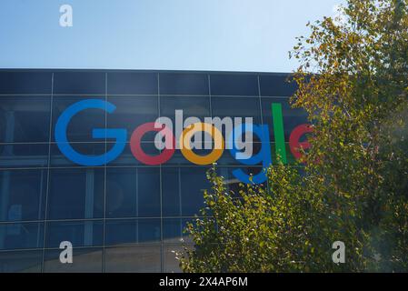 Modern building facade with colorful Google logo, trees, and blue sky reflection. Stock Photo