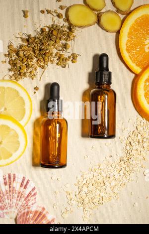 Two brown bottles of essential oil with dropper, sitting on a natural cotton surface and surrounded by the oils' ingredients: fresh orange, lemon and Stock Photo