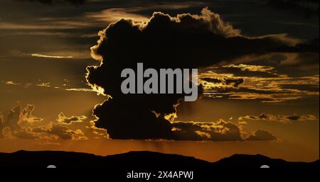 Dreamy thunderhead, beautifully silhouetted, towers above the mountainous desert landscape at sunset. Stock Photo