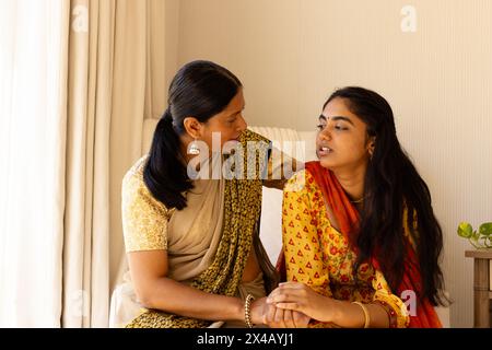 Indian mother in yellow saree comforting teenage daughter, both wearing orange. Both having long black hair, mother showing maturity, sharing quiet mo Stock Photo