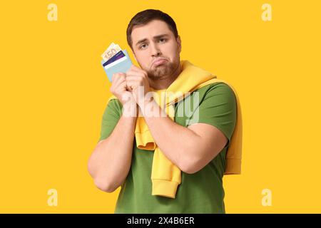 Young upset man holding wallet with credit cards on yellow background Stock Photo