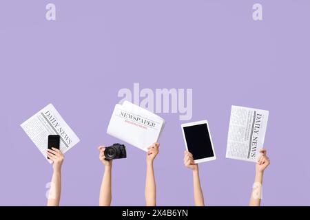 Female hands with newspapers and modern gadgets on lilac background Stock Photo