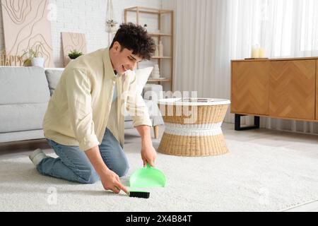 Young man sweeping carpet at home Stock Photo