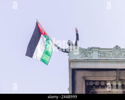 NEW YORK, N.Y. – April 30, 2024: A demonstrator waves a Palestinian flag on the roof of Hamilton Hall at Columbia University in Manhattan. Stock Photo