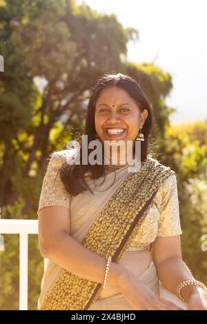 Indian woman wearing sari standing outside, laughing. She has dark hair, brown eyes, and mature skin showing joy, unaltered Stock Photo