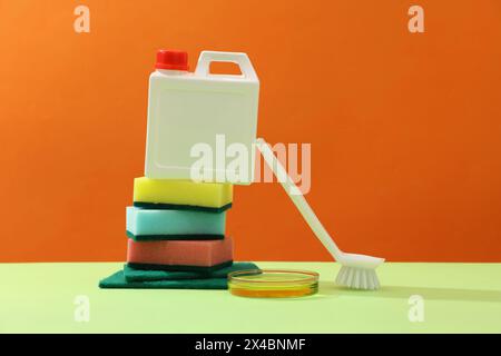 Creative background for advertising detergent products. Stack of sponges and detergent canister decorated with white brush and petri dish of yellow li Stock Photo