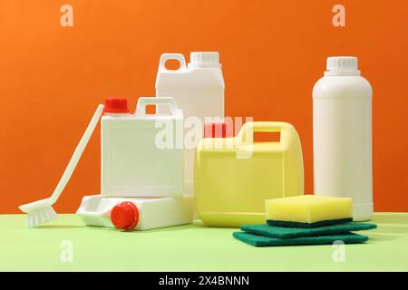 Set of different detergent canisters and bottles decorated with sponges and brush on orange background. Front view, advertising photo for cleansing pr Stock Photo