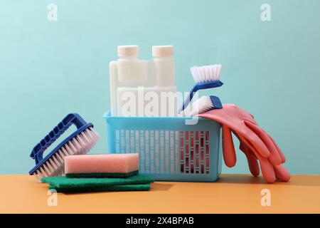 A blue basket with detergents, pink gloves, sponges and brushes on pastel blue background. Front view, minimal scene for advertising with copy space. Stock Photo