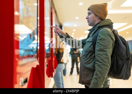 Man interacts with digital kiosk in modern mall, navigating touch screen. Technological integration into shopping experiences. Stock Photo