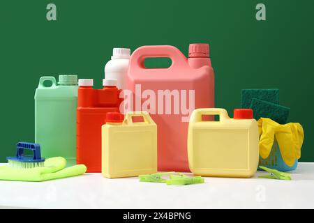 Colorful cleaning set mockup, empty plastic canisters with different sizes and colors decorated with rubber gloves, brush and sponges on dark green ba Stock Photo