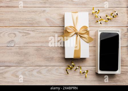 Opened gift box with gold ribbon and smartphone on color background, top view. Blank open box packaging mockup , Template for your design - branding m Stock Photo