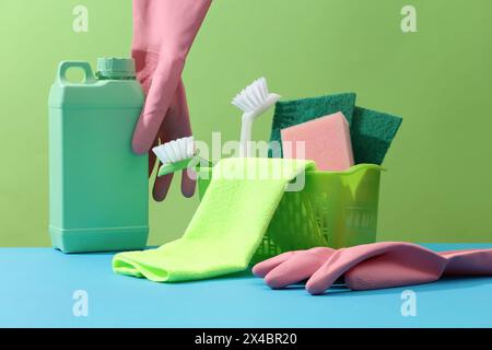 Brushes, sponges, rubber gloves and natural cleaning products in the basket decorated with an empty green bottle on a green background. Front view, mi Stock Photo