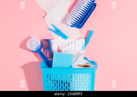 Basket with detergents, gloves, brushes and paper roll decorated on a pink background. Flat lay of cleaning products, advertising photo. Top view, eco Stock Photo