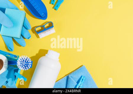 House cleaning product equipment displayed on yellow background. Top view of detergent bottle, blue rubber gloves, sponge, brushes and clothespins. Sp Stock Photo