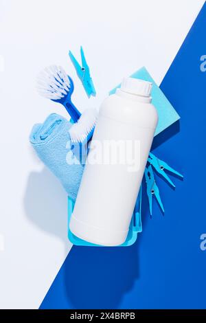 Top view of plastic basket full with wiper, brushes, sponge and clothespins. In the middle is an unbranded white bottle mockup for detergent product a Stock Photo